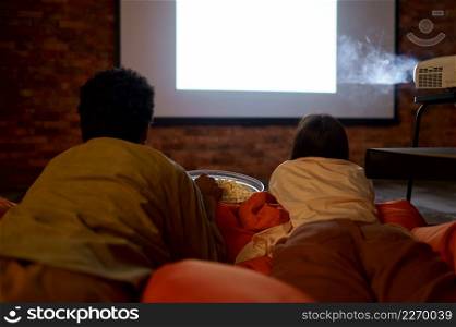 Overhead view on couple lying on soft bag seat watching projector. Cinema for two lovers. Couple lying on soft bag watching projector