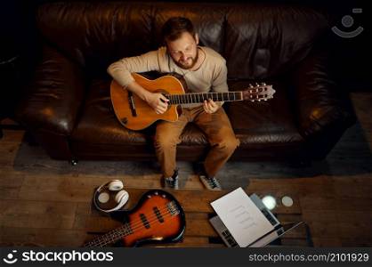 Overhead view on guitarist learning song notes playing guitar sitting on couch front of laptop. Guitarist learning song playing guitar overhead view