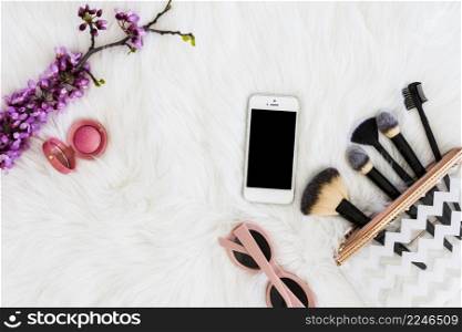 overhead view pink compact face powder with sunglasses mobile phone makeup brush artificial purple twig white fur