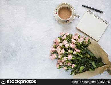 overhead view pink flower bouquet coffee cup spiral notepad pen concrete backdrop