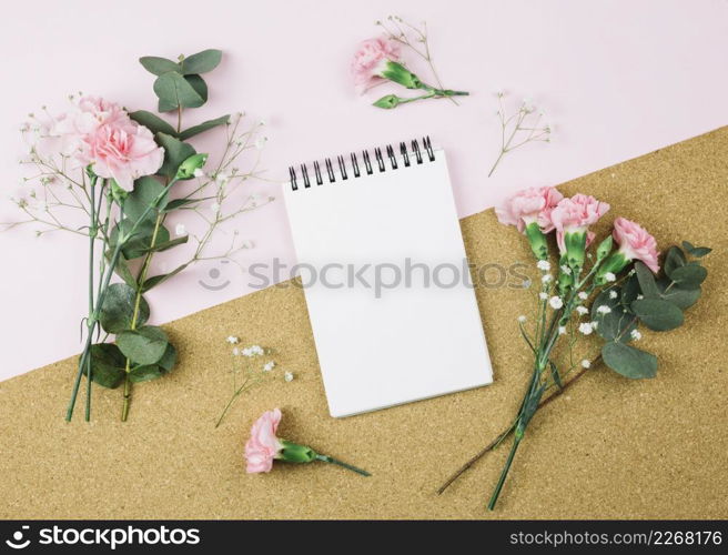 overhead view spiral notepad surrounded with gypsophila carnation flowers dual pink cardboard background