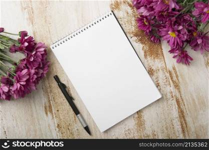 overhead view spiral notepad with pen pink flowers wooden background