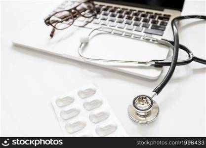 overhead view stethoscope eyeglasses laptop with pill pack white background
