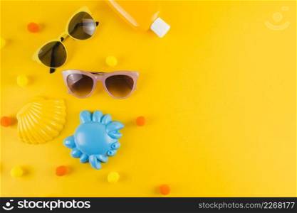overhead view sunglasses sunscreen lotion bottle scallop crab toy yellow backdrop