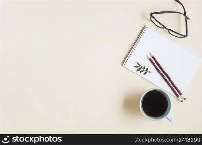 overhead view tea cup eyeglasses pencil spiral notepad against beige backdrop