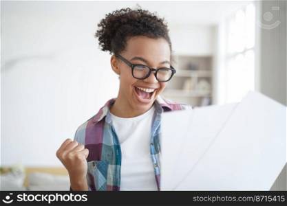 Overjoyed african american high school girl student celebrates success, makes yes gesture, reading letter with positive exam scores. Screaming happy schoolgirl in glasses holds document with good news. Happy african american girl student celebrating achievement, holding document, makes yes gesture