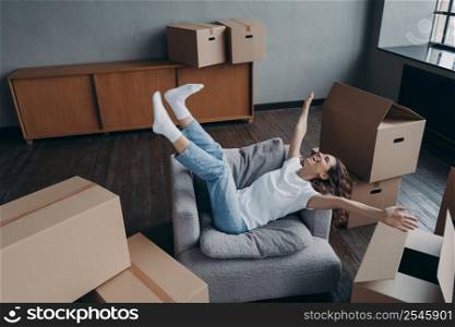 Overjoyed european woman has bought a new house. Spanish young lady relaxing in armchair among boxes. Concept of opportunity for woman and mortgage. Independence and new lifestyle.. Overjoyed european woman has bought a new house. Concept of opportunity for woman and mortgage.