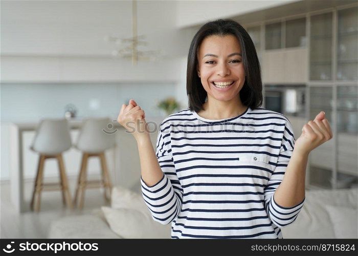 Overjoyed female homeowner makes yes winner hand gesture, celebrating relocation to new home apartment. Young woman rejoices feels happiness with personal achievement, success, good news.. Happy female homeowner makes yes gesture, celebrating achievement, successful relocation to new home