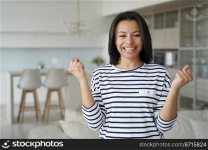 Overjoyed female homeowner makes yes winner hand gesture, celebrating relocation to new home apartment. Young woman rejoices feels happiness with personal achievement, success, good news.. Happy female homeowner makes yes gesture, celebrating achievement, successful relocation to new home