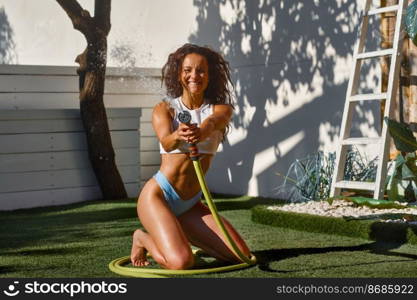 Overjoyed woman playing with spraying garden hose during hot∑mer day on vacation. Overjoyed woman playing with spraying garden hose