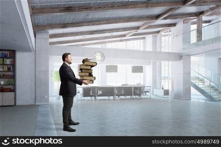 Overloaded with work. Young businessman in modern office carrying pile of books