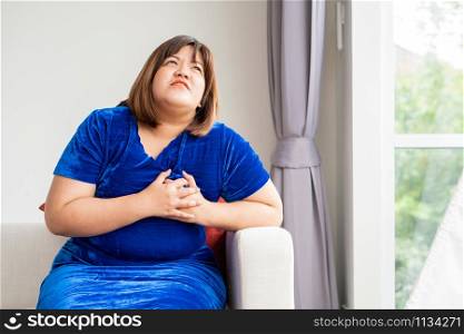 Overweight Asian women are sitting on the sofa in the living room. And handles in the chest due to heart disease, illness, and health care concept.