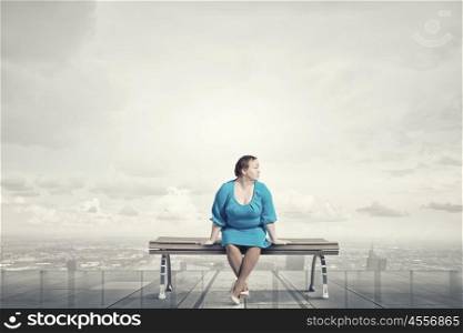 Overweight problem. Middle aged stout woman in blue dress sitting on bench