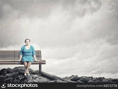 Overweight problem. Middle aged stout woman in blue dress sitting on bench