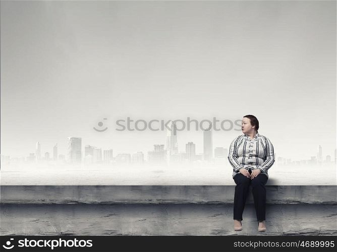 Overweight problem. Middle aged stout woman sitting on building roof