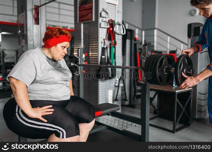 Overweight sweaty woman on workout with barbell in gym. Calories burning, obese female person in sport club