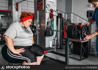 Overweight sweaty woman on workout with barbell in gym. Calories burning, obese female person in sport club