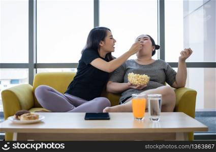 Overweight woman and asian girl enjoy eating food on sofa at home