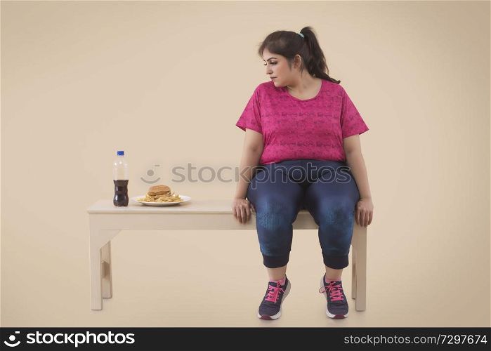 Overweight Woman is looking at the hamburger while resting aftre workout