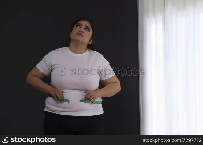 Overweight woman measuring her waist with a tape measure
