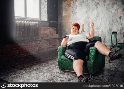 Overweight woman sits in a chair and watches TV. Unhealthy lifestyle, obesity. Overweight woman sits in a chair and watches TV