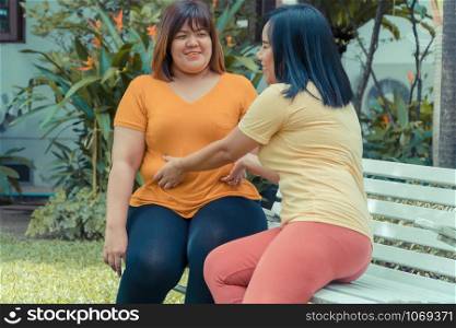 Overweight woman sitting a chair in the garden and his friend is grabbing his stomach