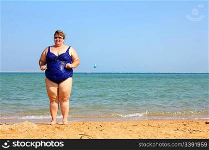 overweight woman standing on beach near sea