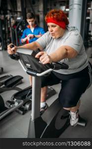 Overweight woman, workout on exercise bike in gym. Calories burning, obese female person in sport club, fat people
