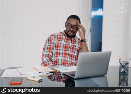 Overworked african american male employee suffers from headache after long working on laptop, sitting at office desk. Tired businessman with closed eyes trying to concentrate to solve problem.. Tired overworked african american male employee suffers from headache after long working on laptop
