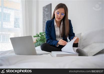 Overworked and Stressed young Asian woman working on laptop computer and document paper in bed at hotel, Business trip, Burnout, technology, copy space, Professional Burnout And Exhaustion Concept.