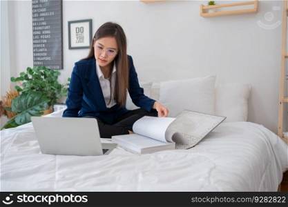 Overworked and Stressed young Asian woman working on laptop computer and document paper in bed at hotel, Business trip, Burnout, technology, copy space, Professional Burnout And Exhaustion Concept.