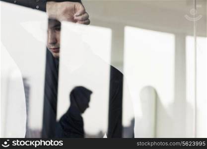Overworked businessman with arm raised leaning on the other side of a glass wall