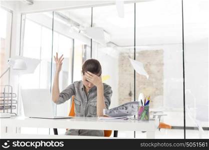 Overworked businesswoman throwing documents at desk in office