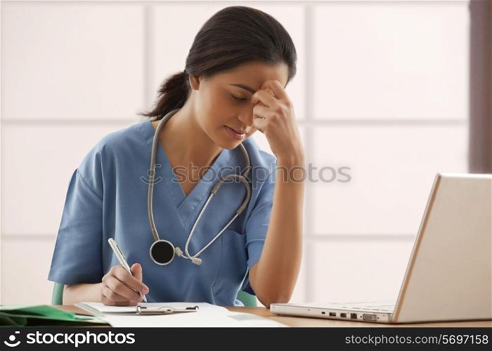 Overworked female surgeon writing notes at desk