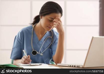 Overworked female surgeon writing notes at desk