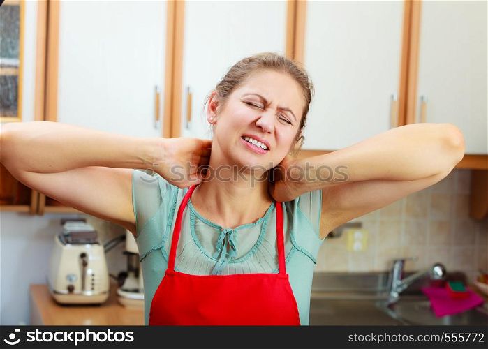 Overworked mature woman suffering from neck pain. Stressed female in kitchen.. Overworked woman suffering from neck pain.
