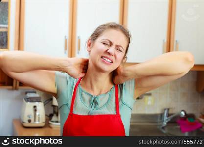 Overworked mature woman suffering from neck pain. Stressed female in kitchen.. Overworked woman suffering from neck pain.