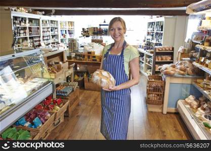 Owner Of Delicatessen Standing In Shop Holding Loaf Of Bread