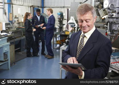 Owner Of Engineering Factory Using Digital Tablet With Staff In Background