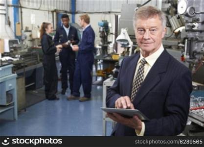 Owner Of Engineering Factory Using Digital Tablet With Staff In Background