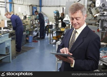 Owner Of Engineering Factory Using Digital Tablet With Staff In Background