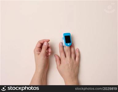 oximeter on a female finger, beige background. Blood oxygen measurement process, top view
