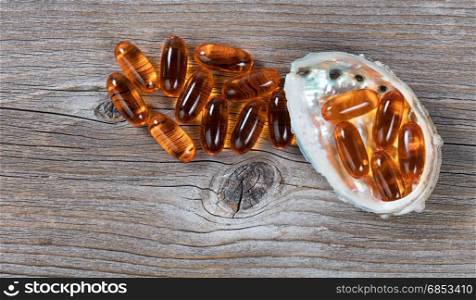Pacific salmon fish oil capsules and seashell on rustic wood. Flat lay view.