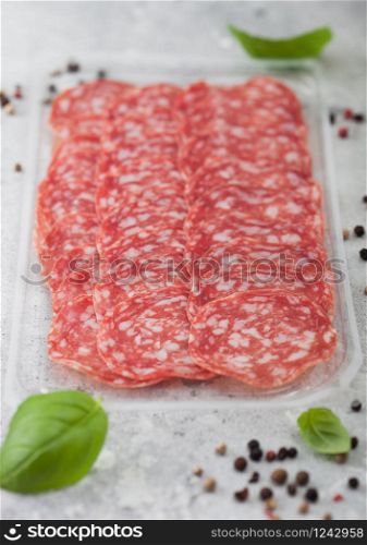 Pack of lassic salami slices with basil and pepper on light background.