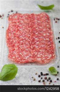 Pack of lassic salami slices with basil and pepper on light background.