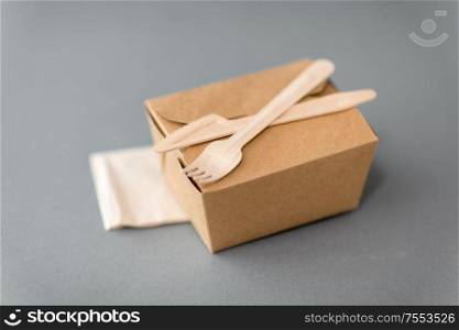 package, recycling and eating concept - disposable box for takeaway food with wooden fork, knife and napkin on table. disposable paper box for takeaway food
