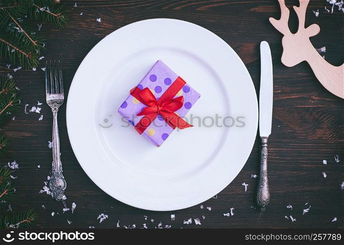 Packed gift on white empty plate, brown vintage in a festive table serving, top view