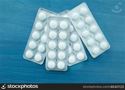 Packings of white pills of medicines on a blue wooden background.