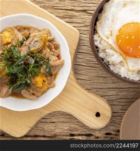 Pad Ka Prao Kai Yeow Ma, Thai food,basil stir fried century egg and sliced pork beside streamed rice with fried egg and sesame on top on rustic natural wood texture background, top view