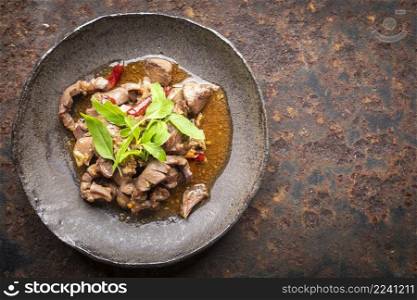Pad Ka Prao Kruang Nai Gai, Thai food, basil stir fried chicken offal, variety meats, pluck or organ meats in wabi sabi style plate on rusty texture background with copy space for tex, top view